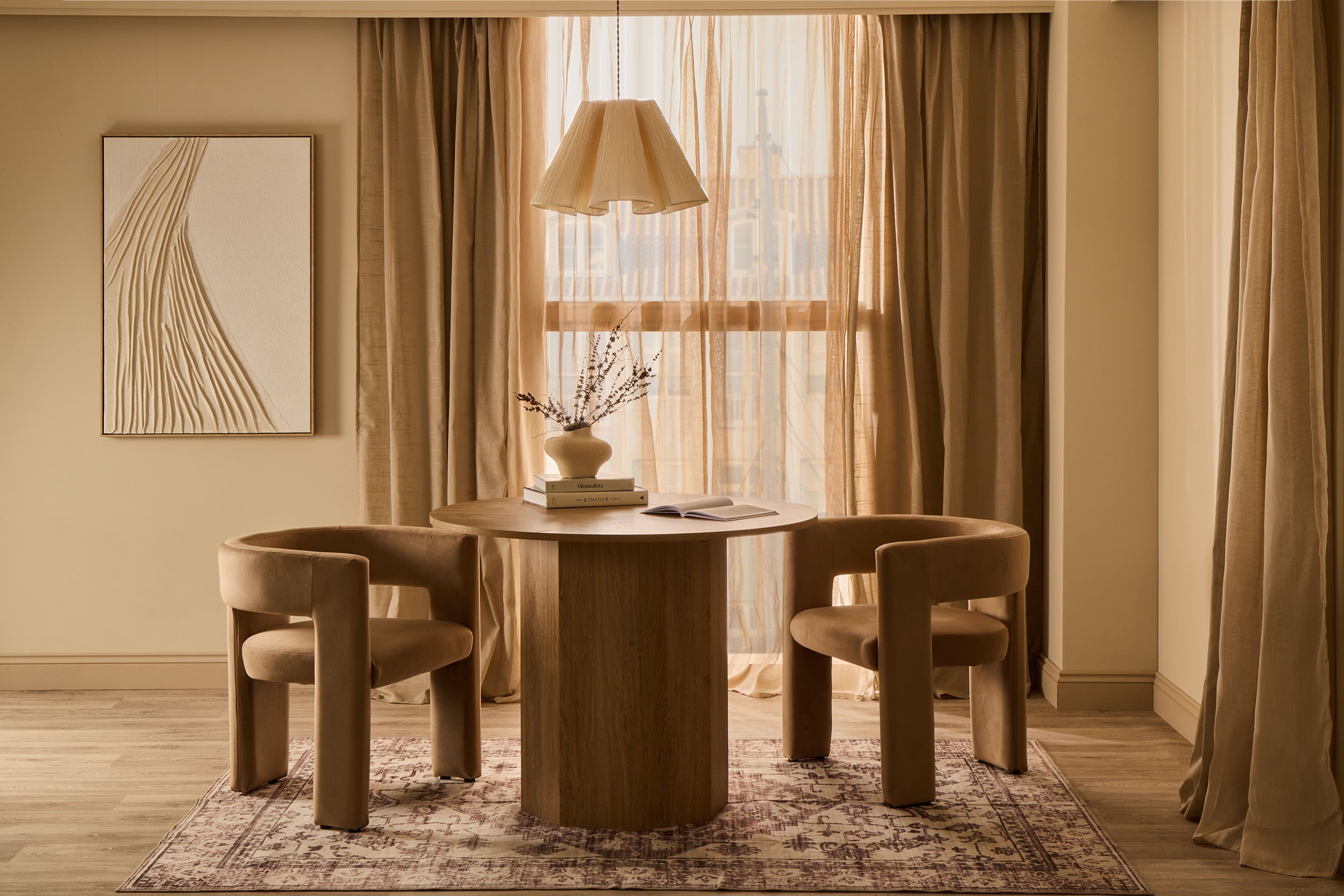 Round wooden dining table with curved upholstered chairs, sheer curtains and warm natural light.