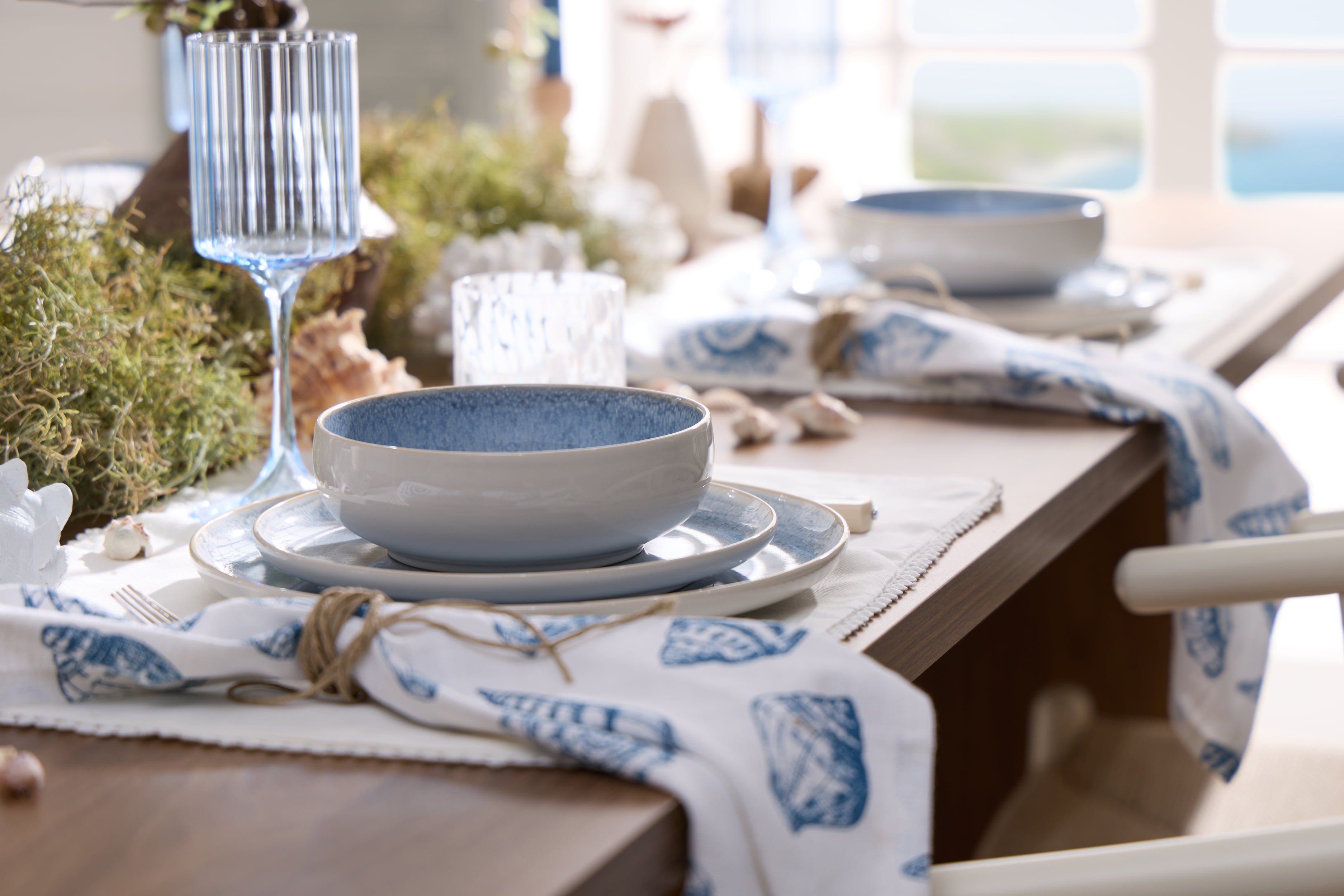 Coastal dining table styled with blue stoneware plates, blue glassware and shell print table linen